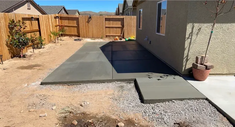 A concrete walkway is being built in the backyard of a house.