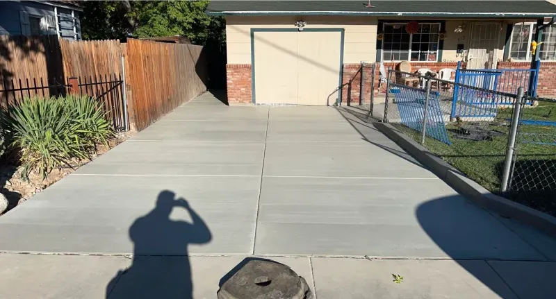 A shadow of a person is cast on a concrete driveway in front of a house.
