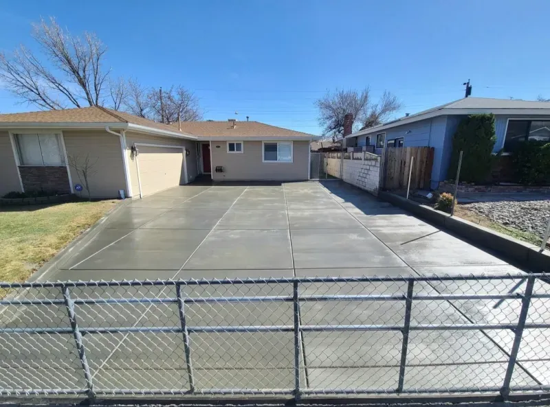 A concrete driveway in front of a house with a chain link fence.
