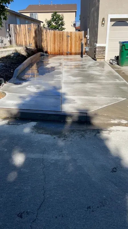 A concrete driveway is being built in front of a house with a wooden fence.