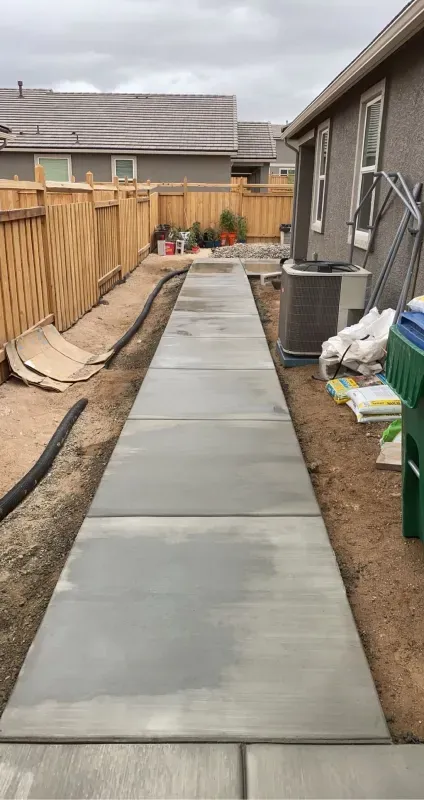 A concrete walkway is being built in the backyard of a house.