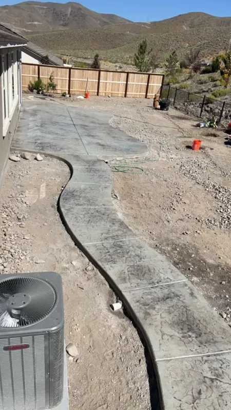 A concrete walkway is being built in the backyard of a house.