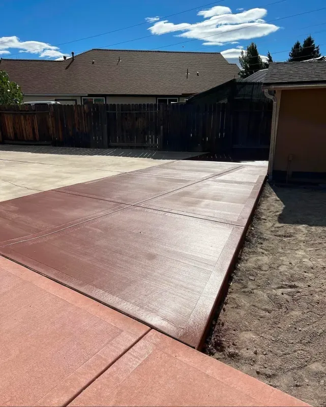 A concrete driveway with a fence in the background and a house in the background.