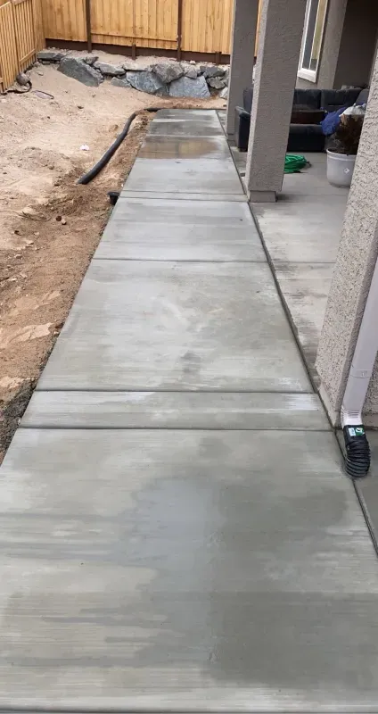 A concrete walkway is being built in the backyard of a house.