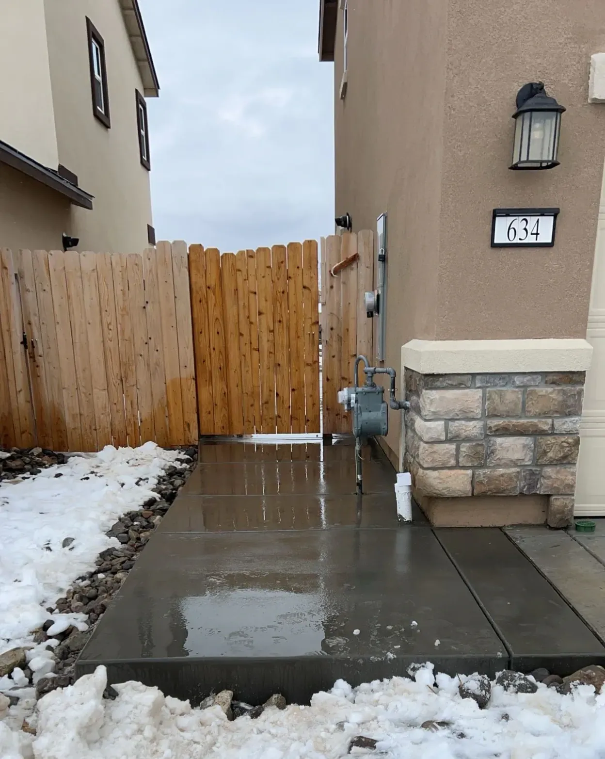 A concrete walkway leading to a house with a wooden fence