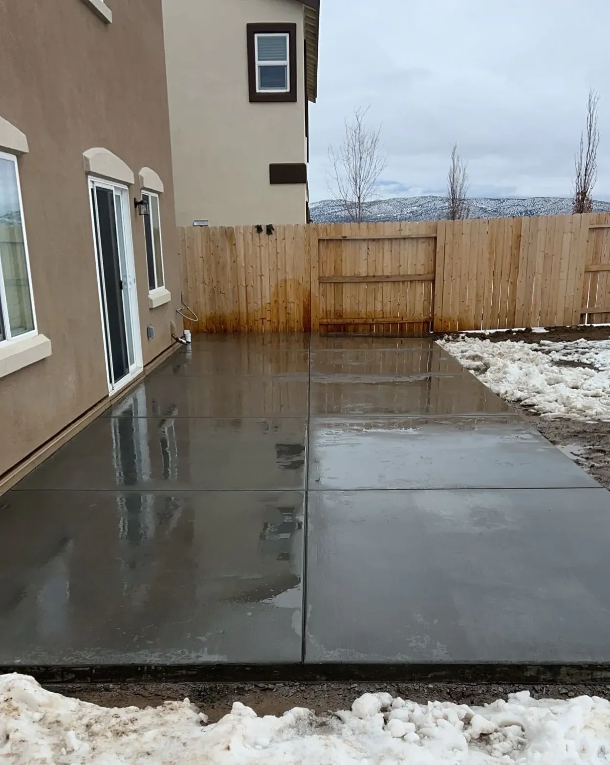 A large concrete patio in front of a house with a wooden fence.