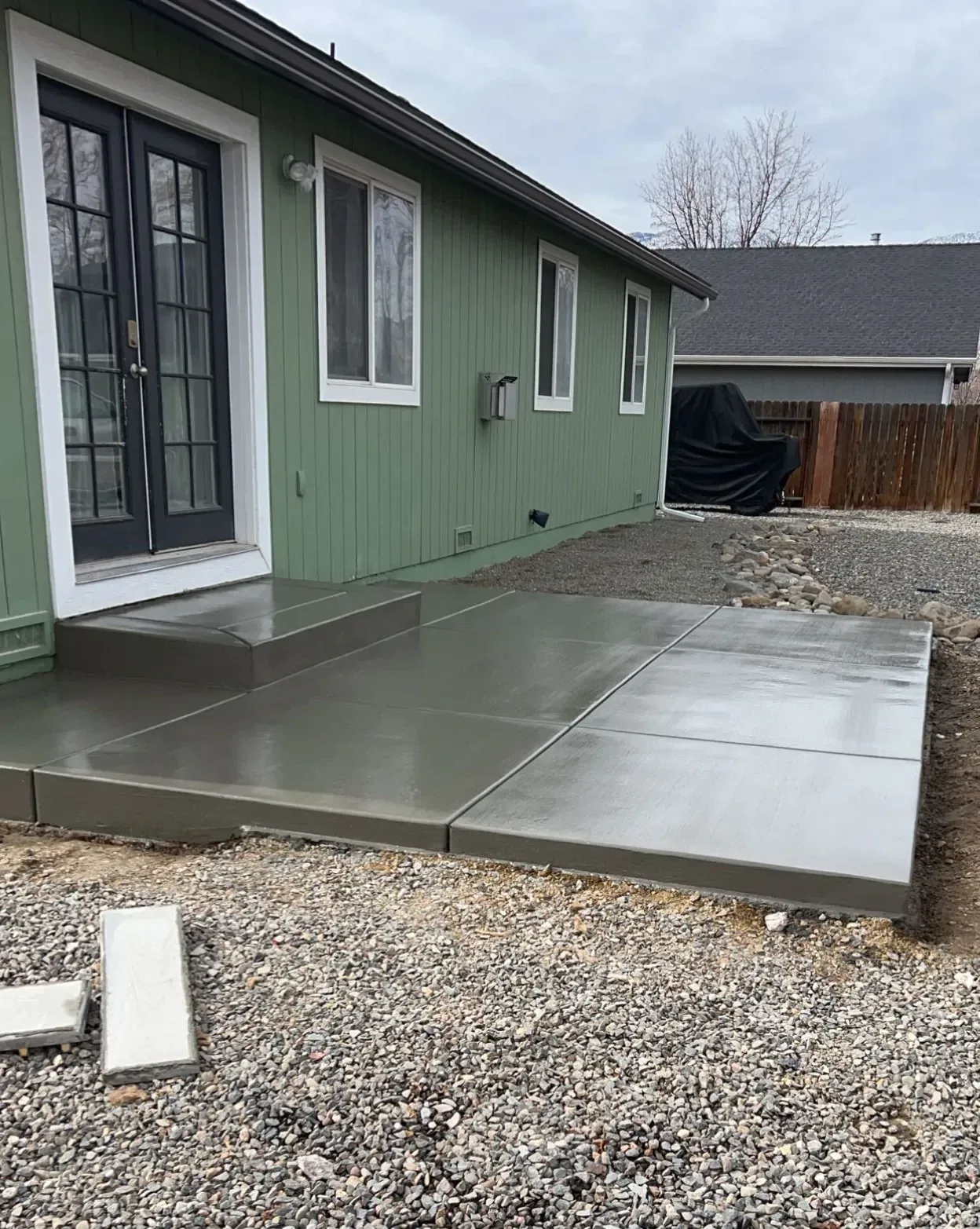 A green house with a concrete patio in front of it.