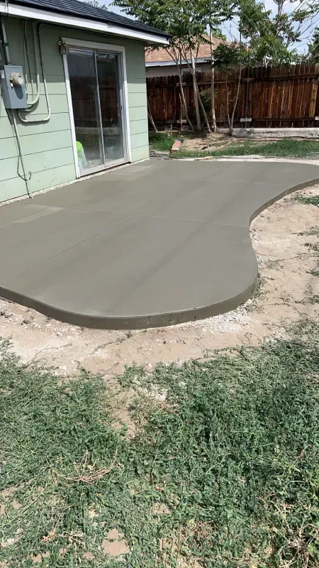 A concrete patio is being built in the backyard of a house.