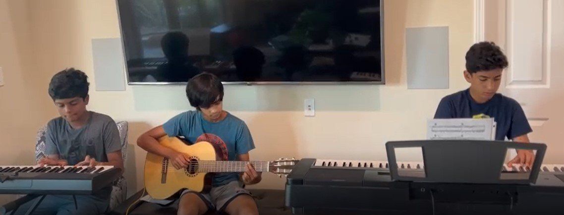 Three young boys are playing guitar and keyboards in a living room.