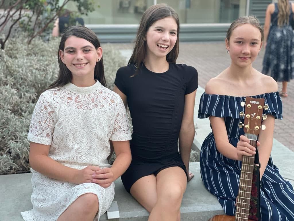 Three young girls are sitting on a bench with a guitar.
