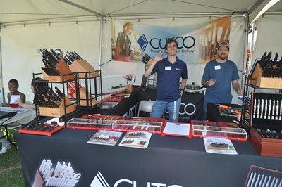 Two men are standing in front of a table filled with knives.