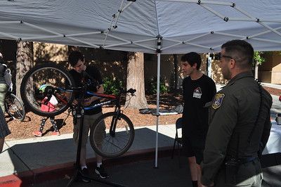 A man is fixing a bike under a tent while a police officer watches.