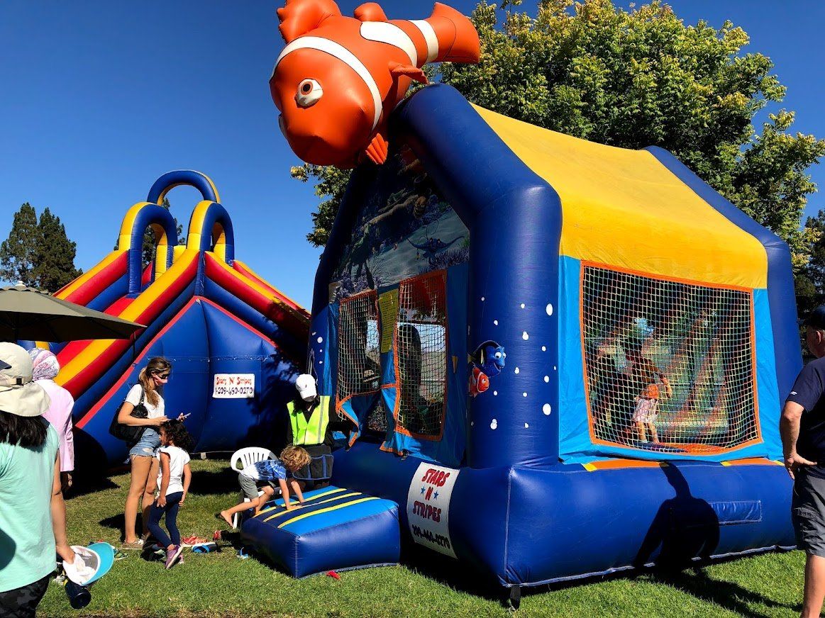 A group of people are standing around a bouncy house with a clown fish on top of it.