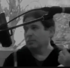 A man is standing in front of a microphone in a black and white photo.