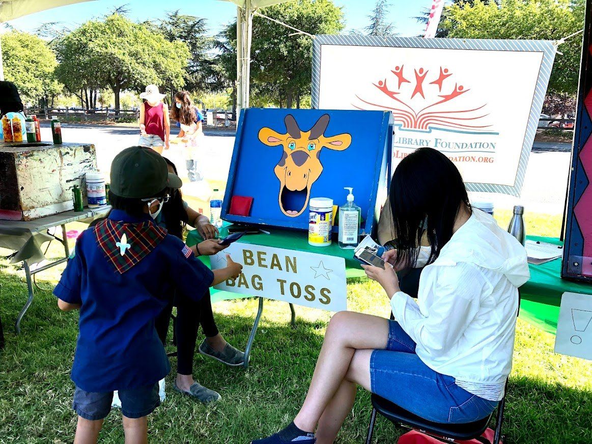 A group of children are playing bean bag toss in a park.