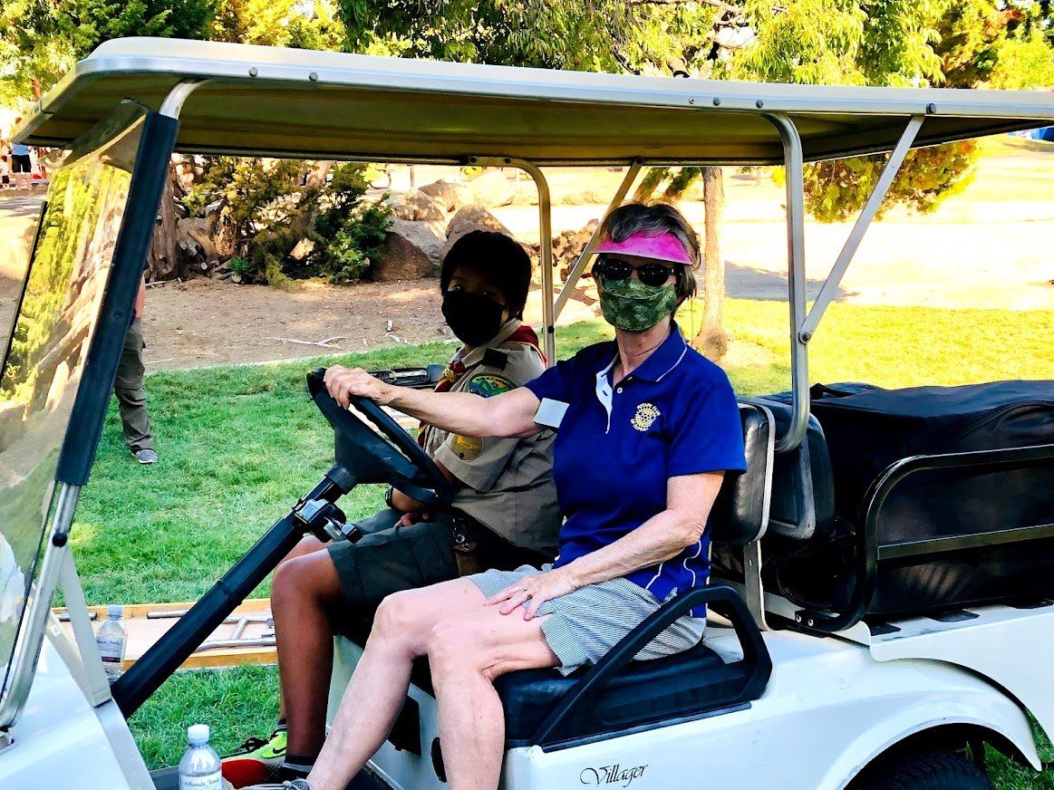 A woman wearing a mask is driving a golf cart with a scout