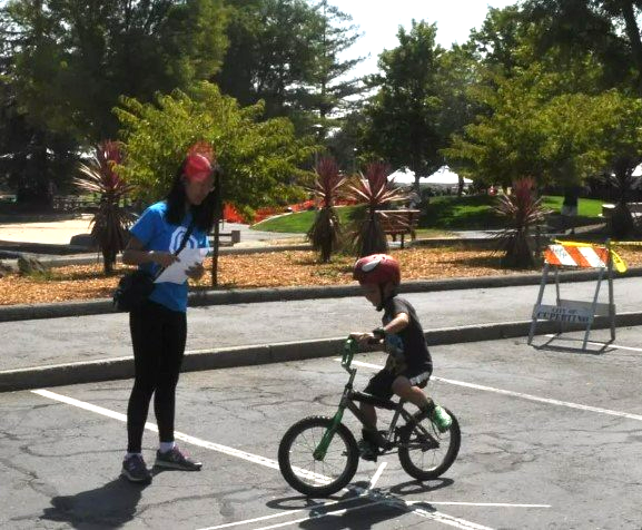 A little boy is riding a bike in a parking lot while a woman watches