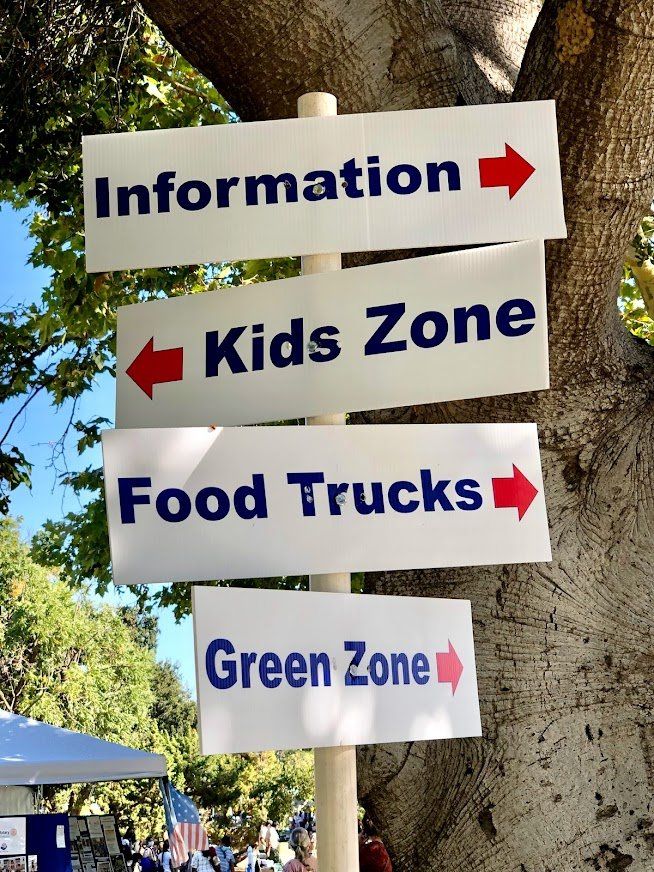 A sign pointing to information kids zone food trucks and green zone