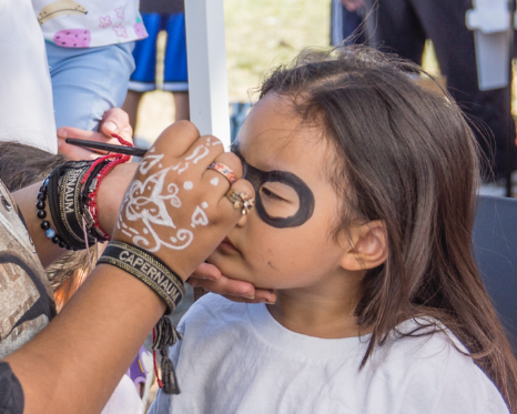A little girl is getting her face painted with purple paint.