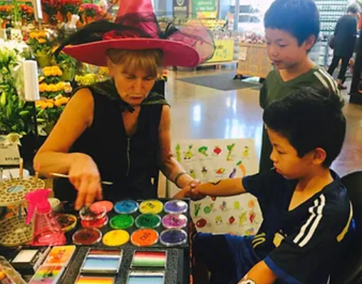 A woman in a witch hat is painting a child 's face