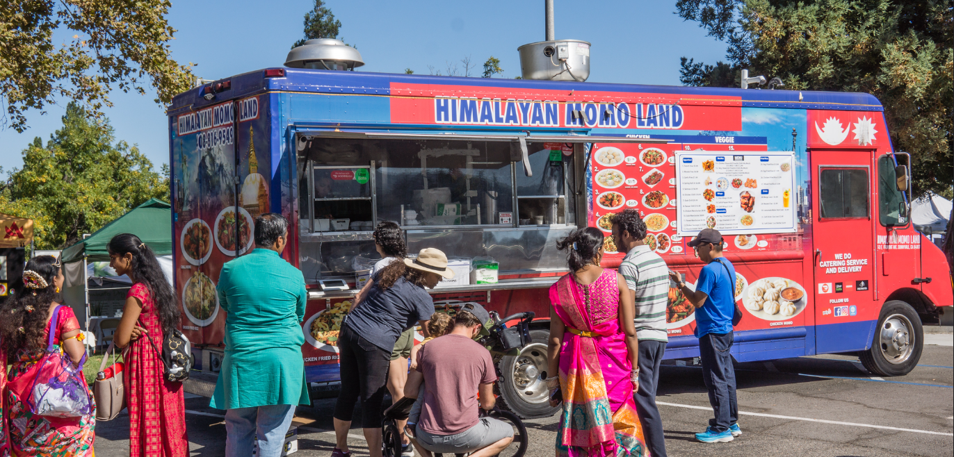 A man is standing in front of a food truck in a parking lot.