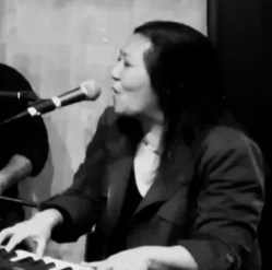 A woman is singing into a microphone while playing a keyboard.