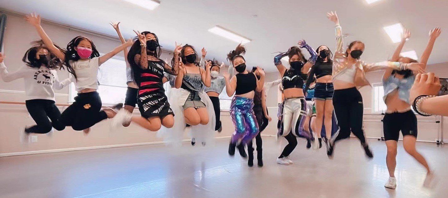 A group of young women are jumping in the air in a dance studio.