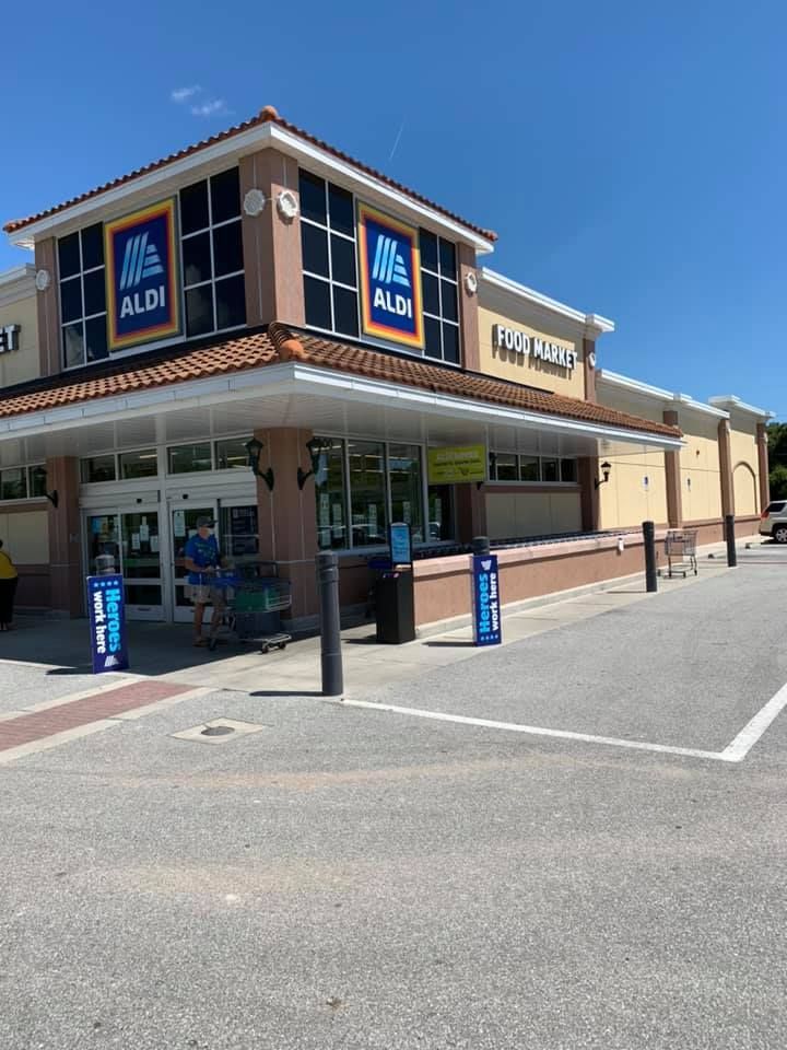 Exterior of an Aldi grocery store. Beige building with large Aldi signs and glass windows on a sunny day.
