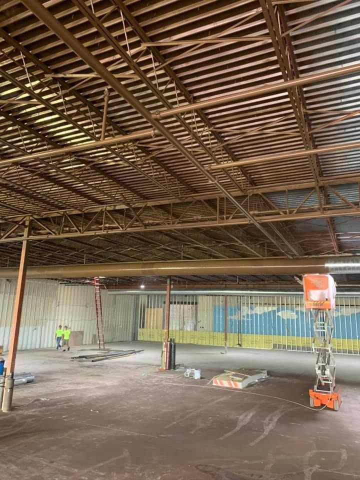 Interior of a construction site with exposed metal beams. Workers, lift, and unfinished walls.