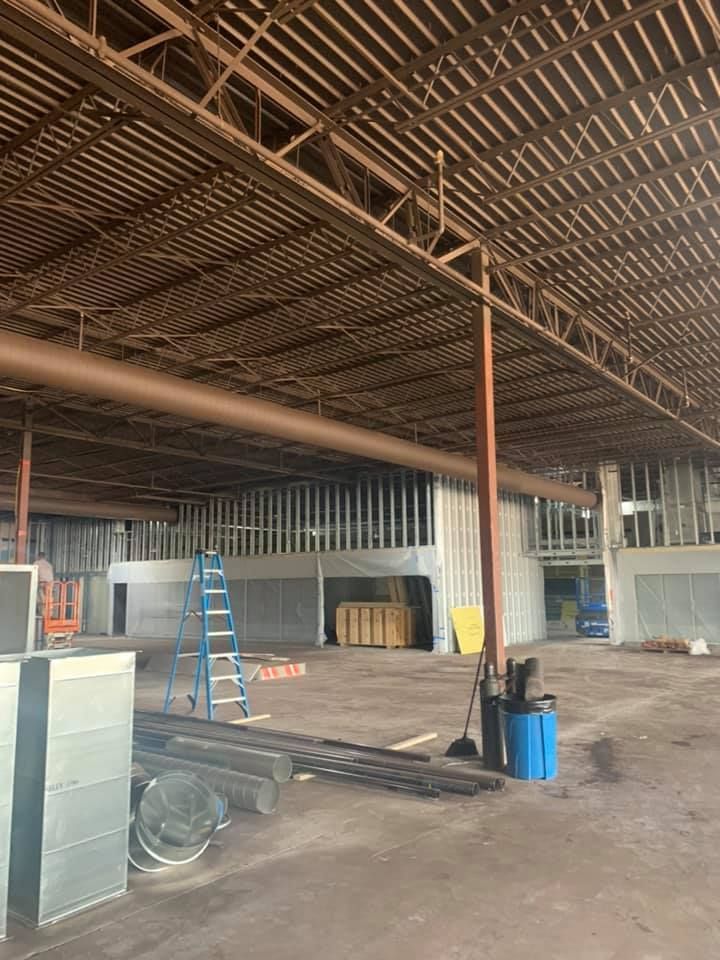 An empty warehouse under construction, with exposed metal beams, wood framing, and scattered construction materials.