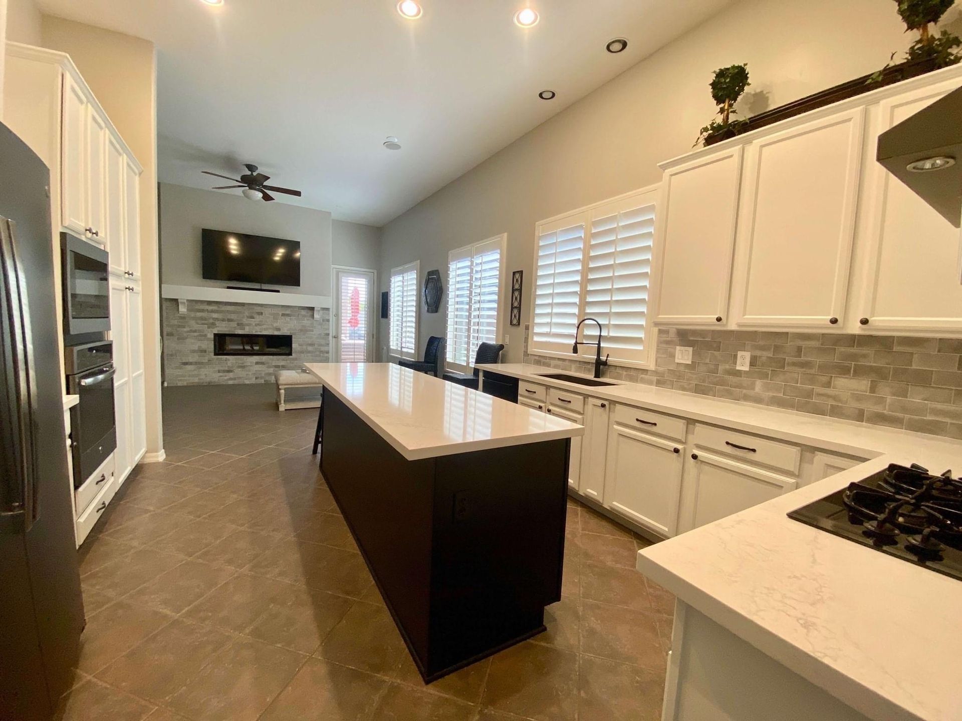 Modern kitchen with white cabinets, dark island, and fireplace in the background.