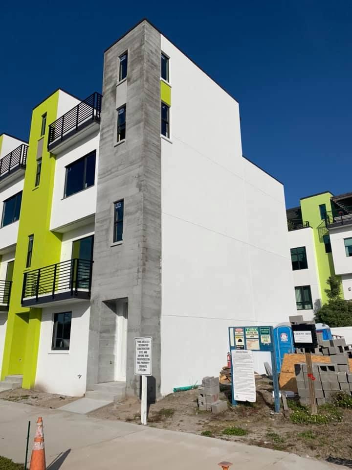 Modern multi-story townhomes, white and lime green accents, under construction.
