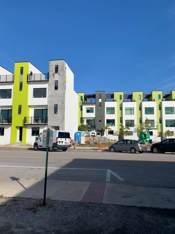 Modern townhouses with lime green and white accents along a street, under a blue sky.