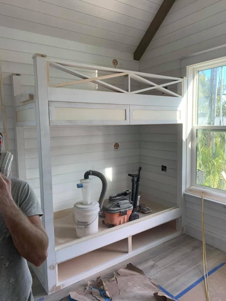 Bunk bed being built in a room with white shiplap walls. Construction tools are visible.