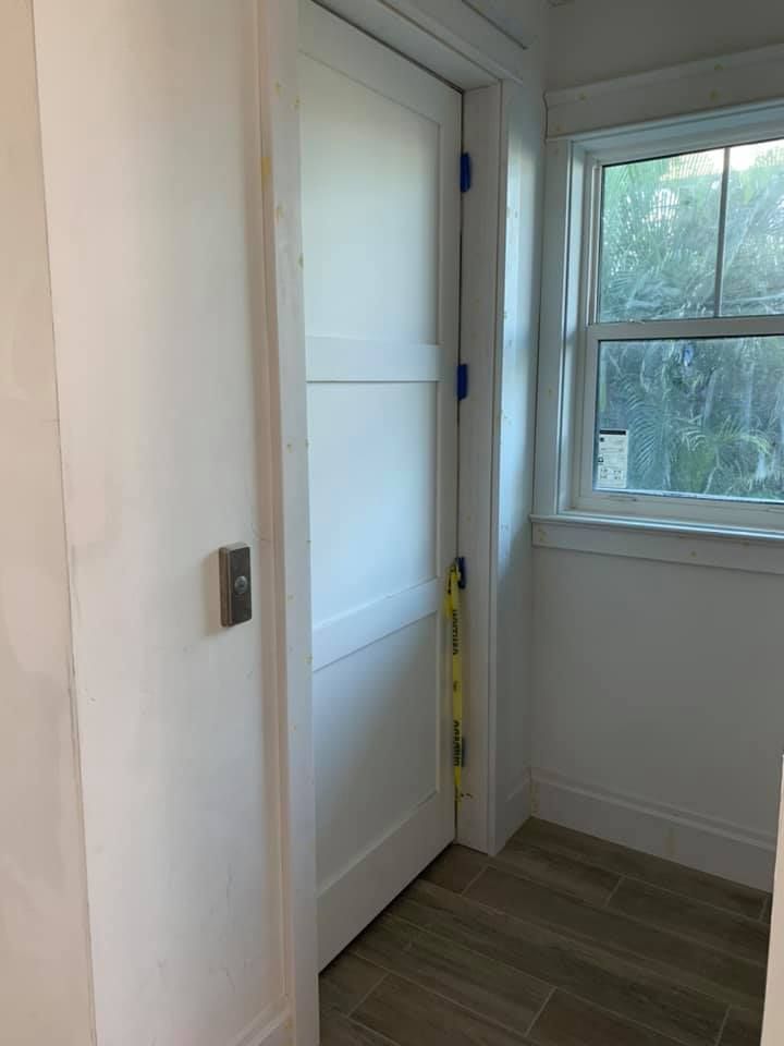 White door slightly ajar, level resting against the side, next to a window.