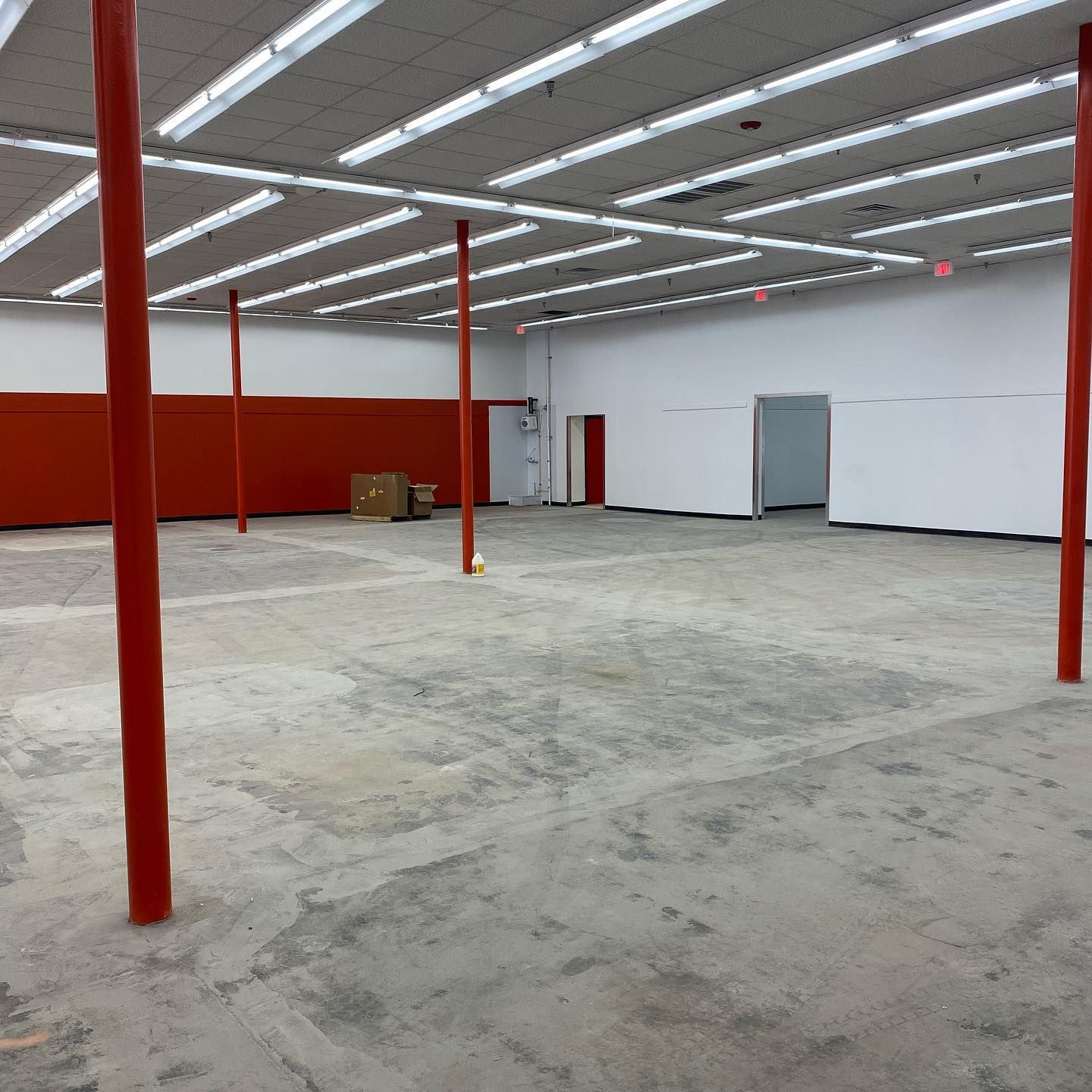 Empty retail space with orange support columns and white walls, concrete floor, overhead fluorescent lights.