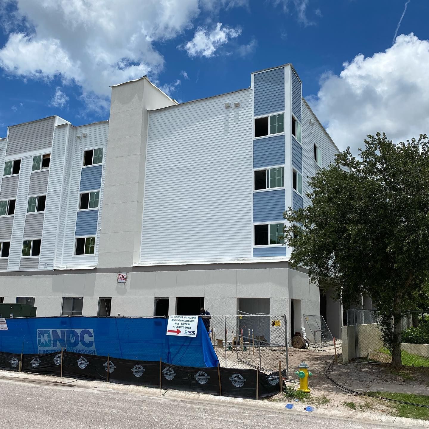 Construction site: multi-story building, white, blue, gray panels; blue barrier in front.