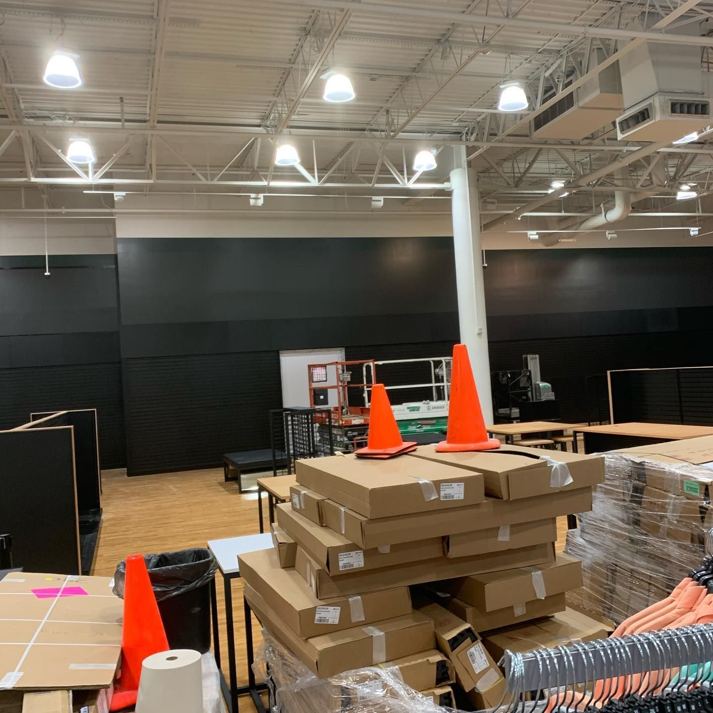 Interior of a large store under construction. Boxes, tables, traffic cones, and black walls are visible.