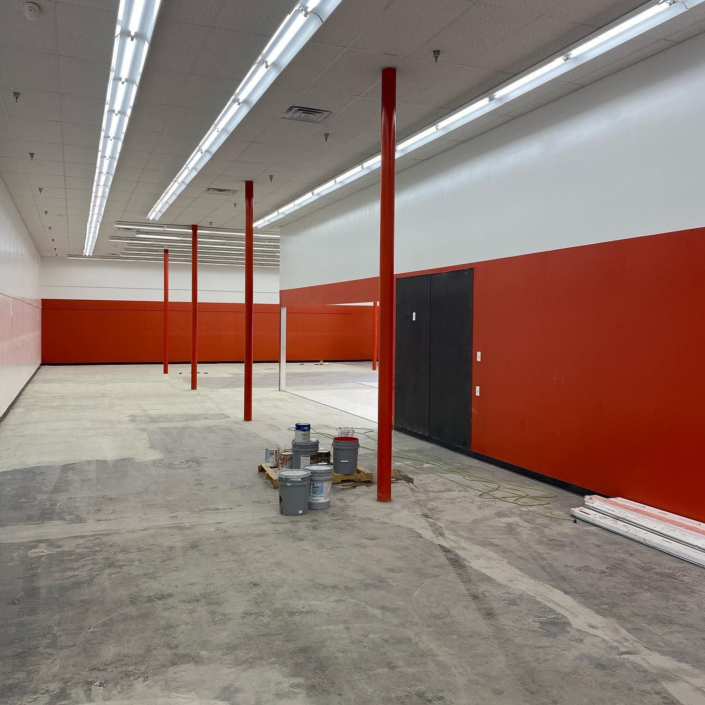 Empty interior of a retail space with red walls, support beams, and concrete floor.