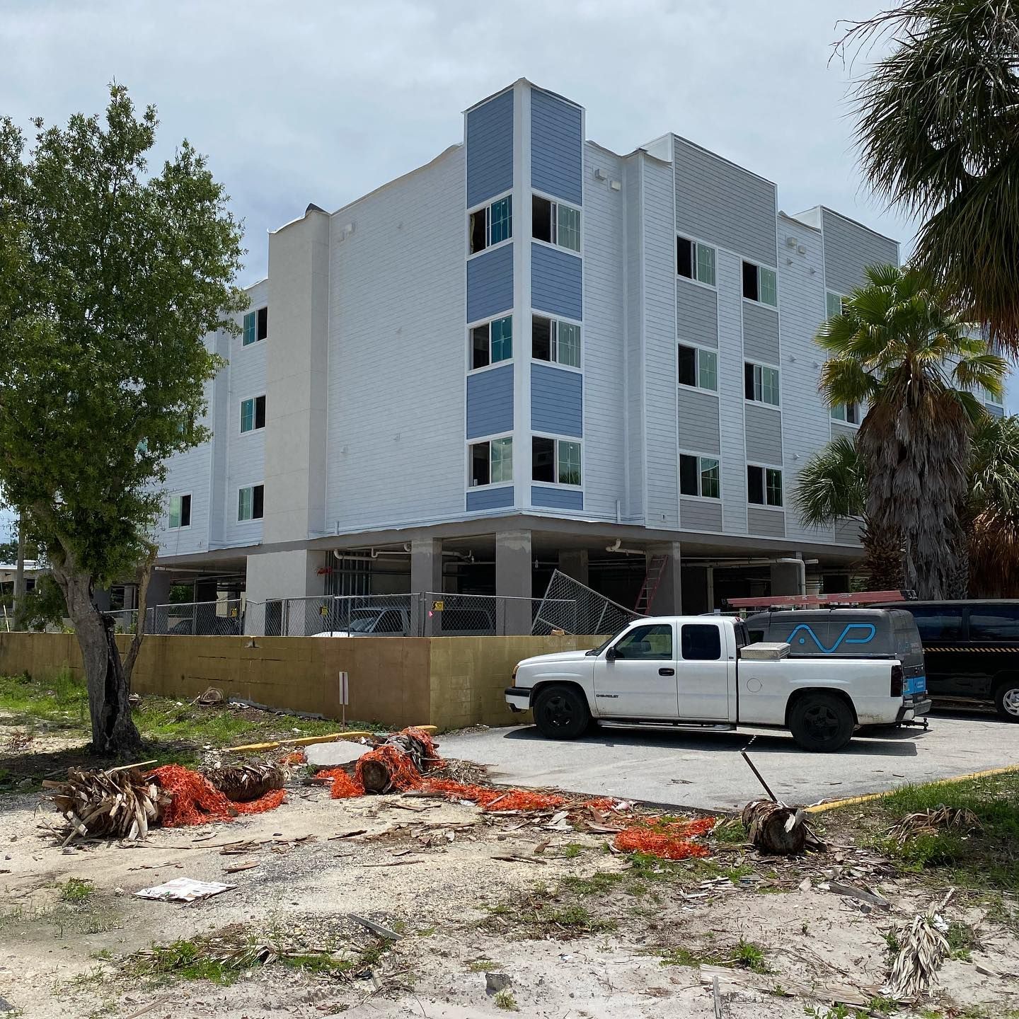 Four-story building with blue and white facade, built on stilts. White pickup truck parked nearby.