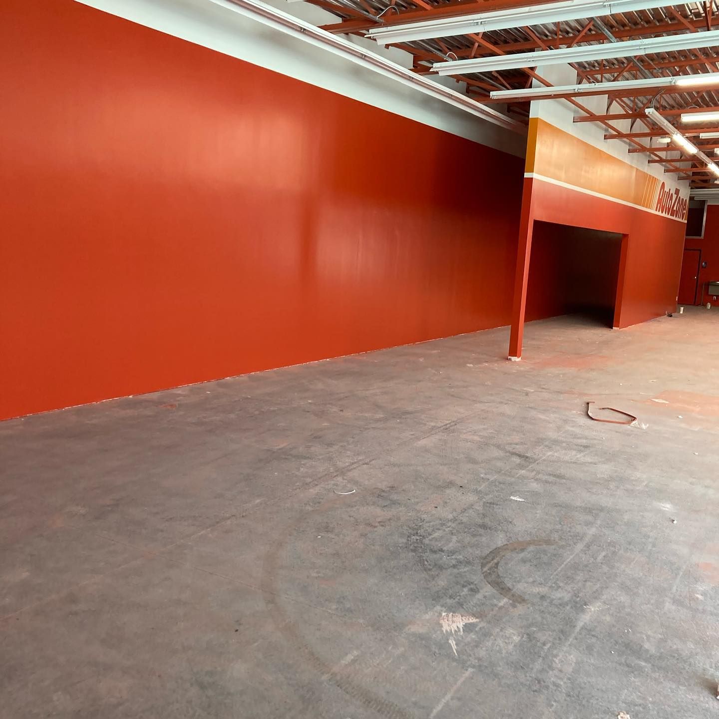 Empty warehouse interior with orange walls, concrete floor, and exposed ceiling beams.