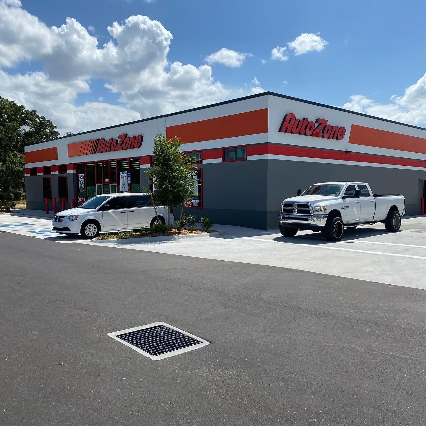 AutoZone store with a white car and pickup truck in the parking lot, sunny day.