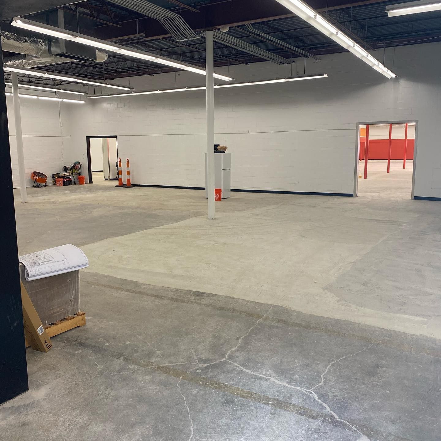 Empty commercial space with white walls, concrete floor, and orange accent room.