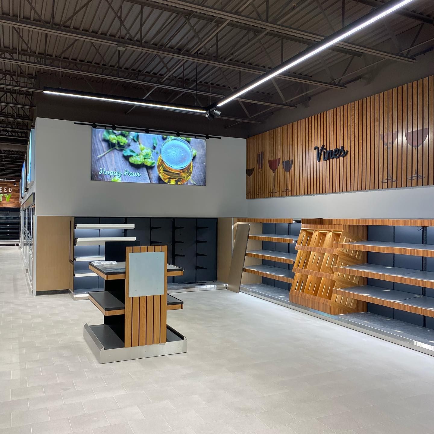 Empty grocery store with wood and metal shelving and a large screen above.