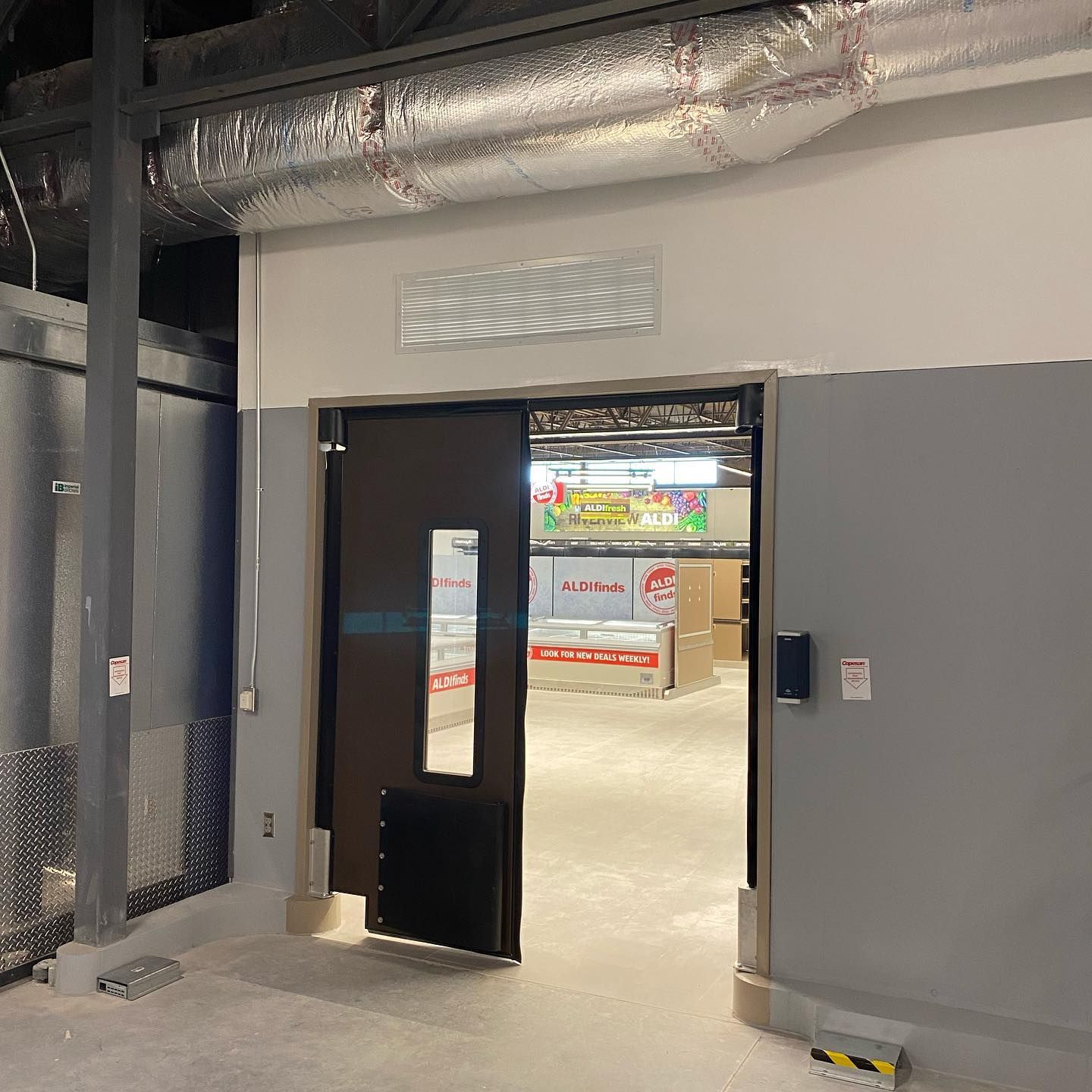 Doorway to a store interior. Brown door, grey walls, open doorway to a brightly lit space with merchandise.
