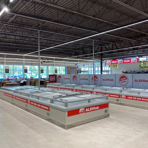 Interior of an Aldi grocery store with refrigerated display cases, gray floor, and high ceiling.