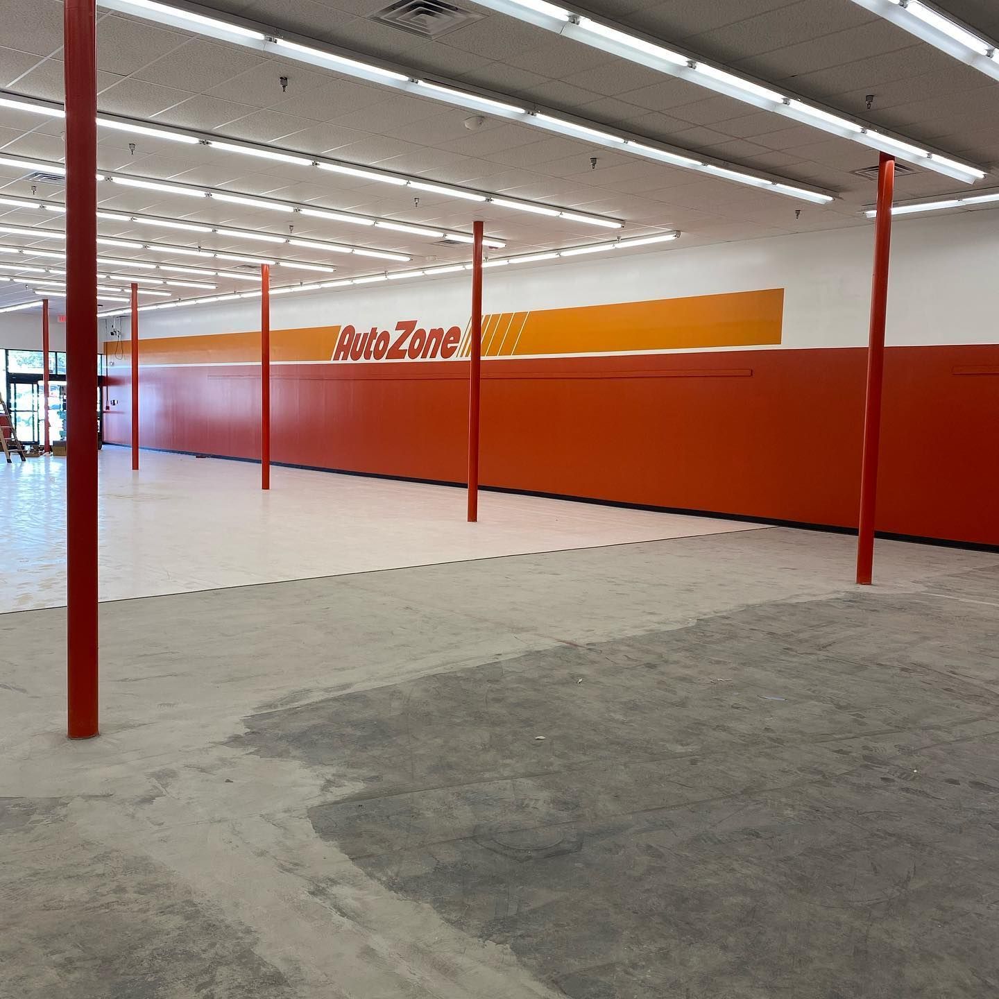 Empty AutoZone store with orange walls, red support poles, and unfinished flooring.