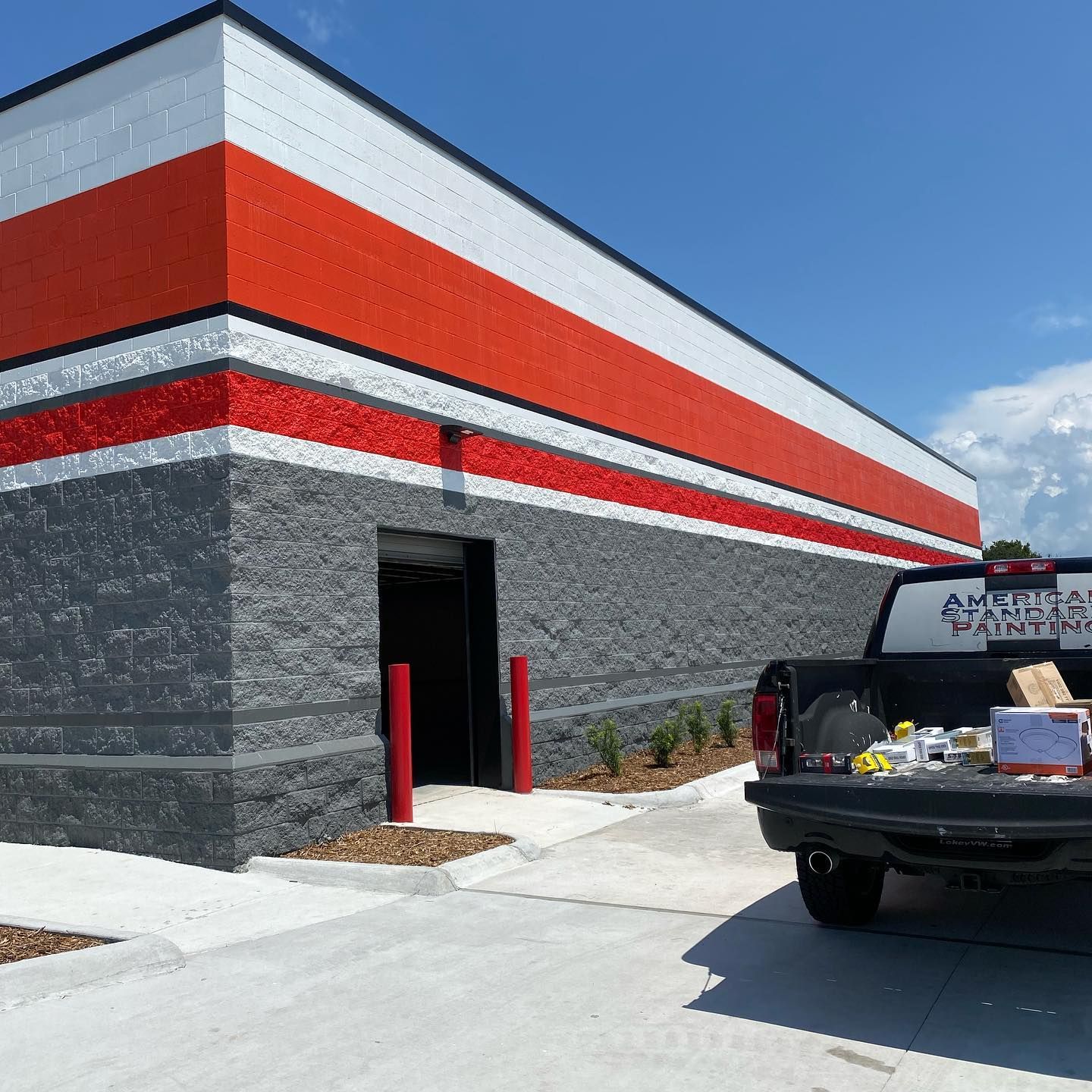 Exterior of building painted gray, white, and red with a truck in front.