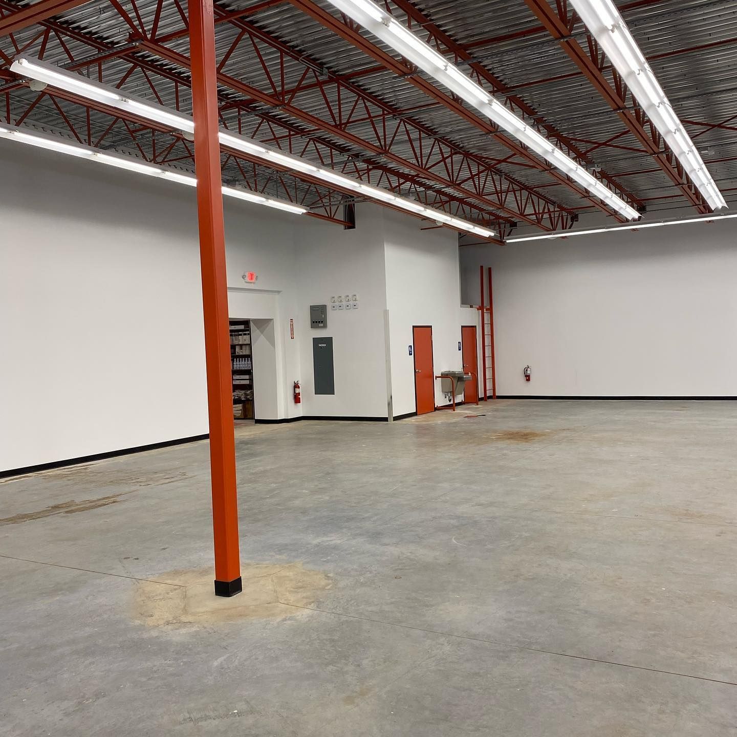 An empty warehouse interior with a red support beam, white walls, and exposed red beams on the ceiling.