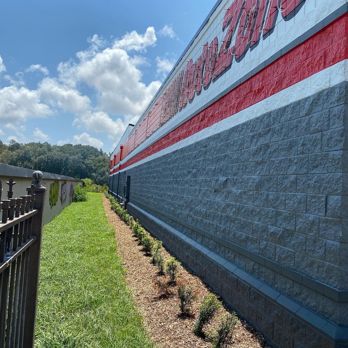 Side view of a gray brick building with a red stripe, trees, grass, and a fence.